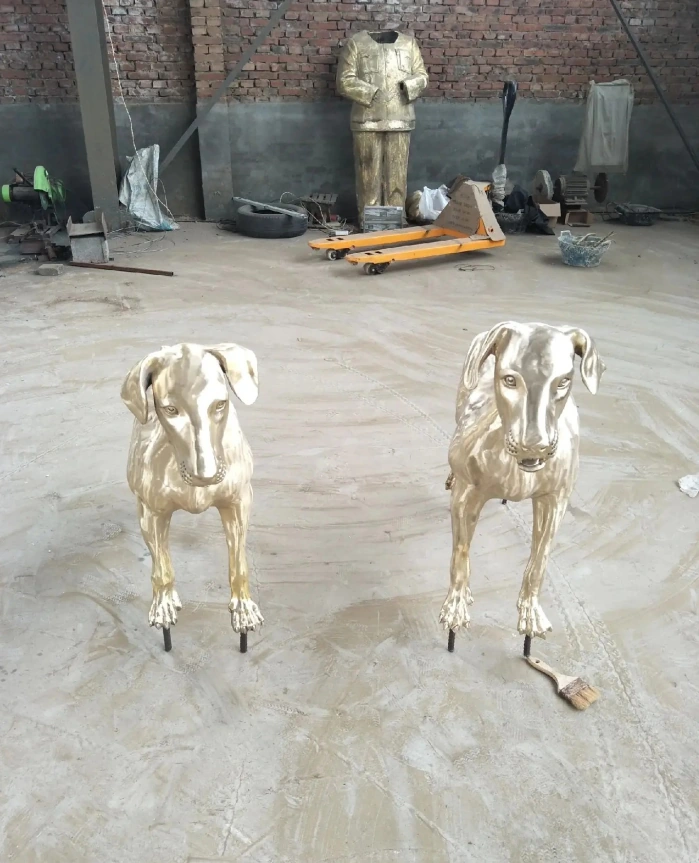 Two standing metal dog sculptures with reflective surfaces and folded ears photographed on the workshop floor.