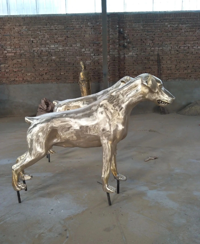 Side view of a standing metal dog sculpture with a reflective surface, folded ears and long legs in the workshop.