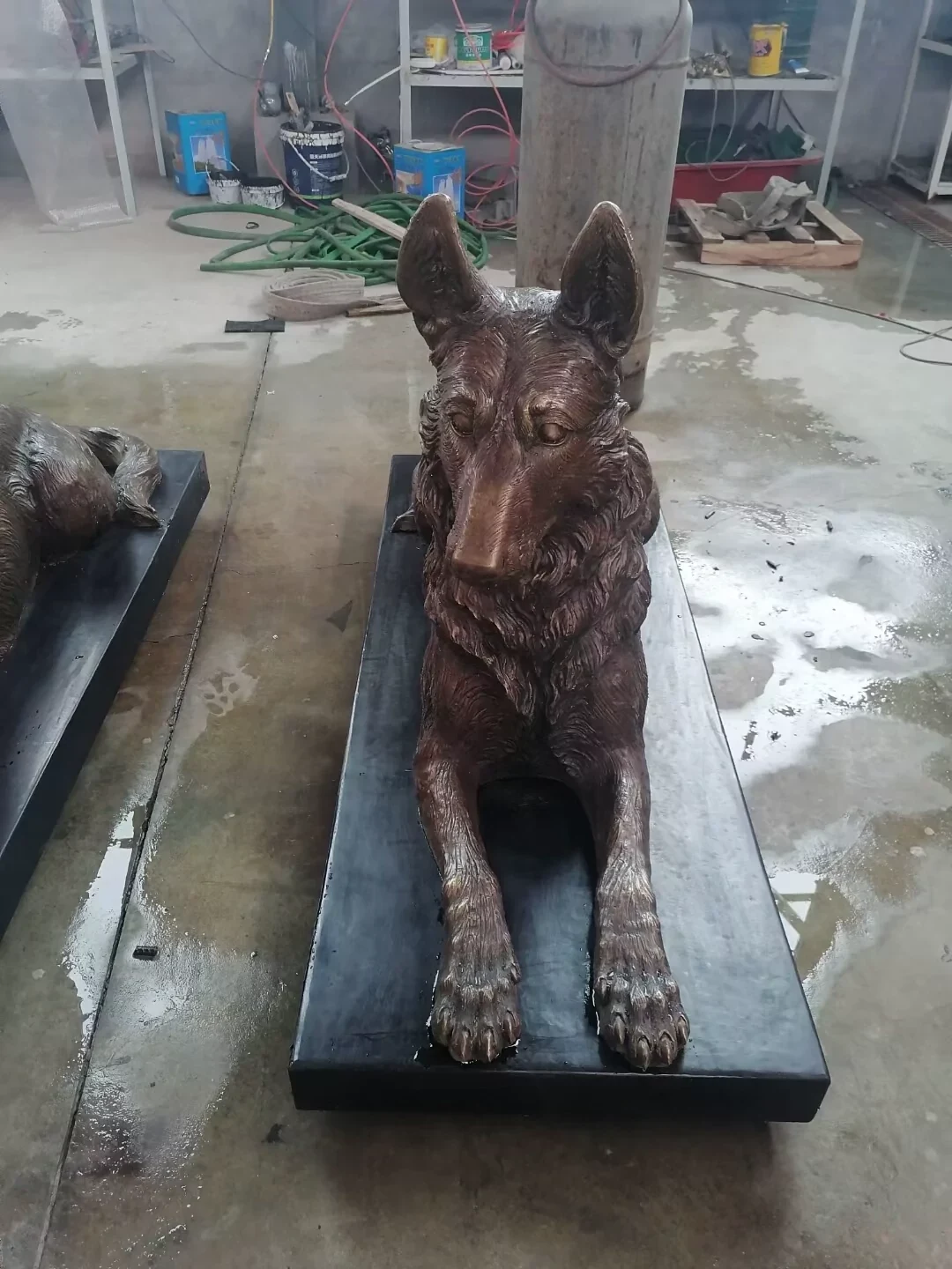 Factory photograph of a reclining German Shepherd sculpture with an upright head on a rectangular base