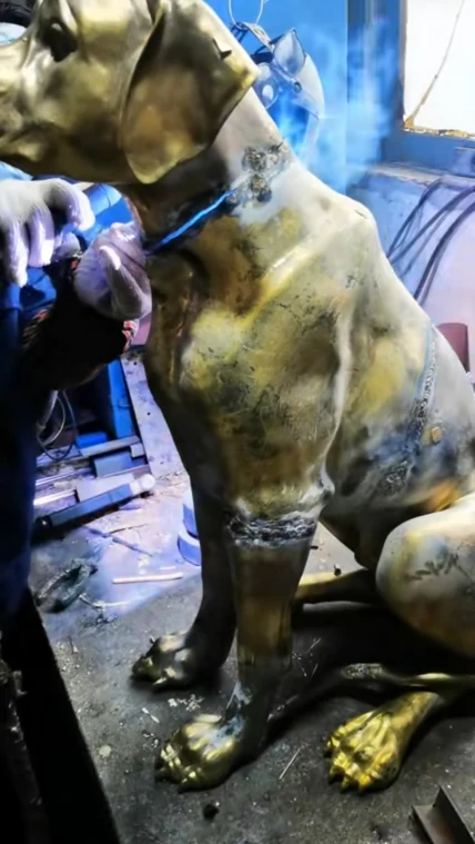 Factory process photograph showing a metal dog sculpture with visible joining work around the neck and body