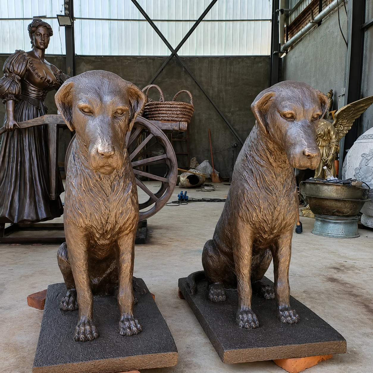 Two seated dog sculptures on individual rectangular bases in a workshop.