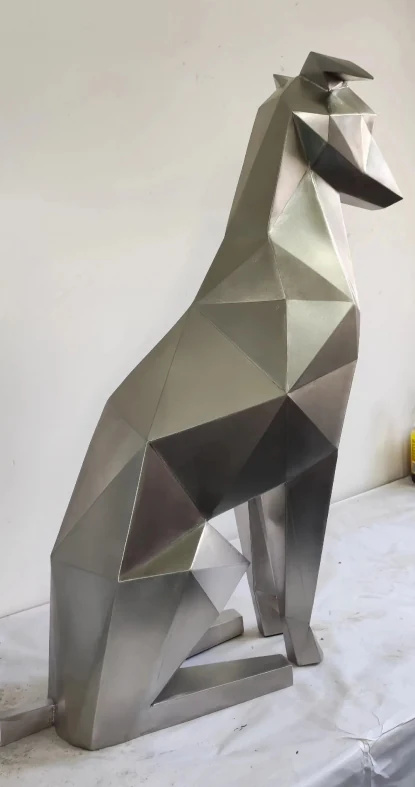 Side view of a faceted seated dog sculpture in brushed 304 stainless steel, photographed in the workshop.